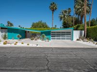 a green house sits in the desert near palm trees and bushes surrounding it's driveway