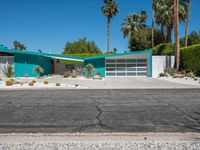 a green house sits in the desert near palm trees and bushes surrounding it's driveway