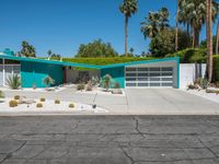 a green house sits in the desert near palm trees and bushes surrounding it's driveway