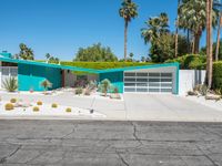 a green house sits in the desert near palm trees and bushes surrounding it's driveway