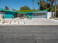 a green house sits in the desert near palm trees and bushes surrounding it's driveway