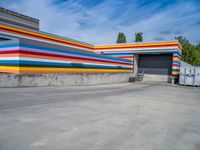 an empty parking lot painted brightly stripes on the wall of the building and sky as well as stones