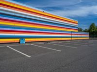 an empty parking lot painted brightly stripes on the wall of the building and sky as well as stones