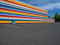 an empty parking lot painted brightly stripes on the wall of the building and sky as well as stones