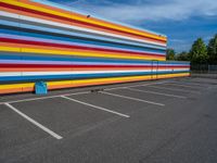 an empty parking lot painted brightly stripes on the wall of the building and sky as well as stones