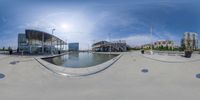 a fish eye view of a pond surrounded by buildings and some water steps and a bridge