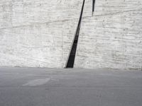 an empty parking lot near a white wall with a concrete pipe sticking out of it