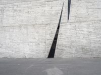 an empty parking lot near a white wall with a concrete pipe sticking out of it