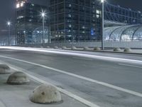 the empty city road is empty by the tall building in the background at night with light streaking on the buildings