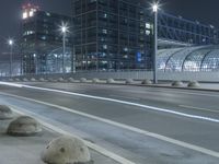 the empty city road is empty by the tall building in the background at night with light streaking on the buildings