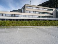 a building sits in a parking lot surrounded by hedges and mountain ranges on the horizon