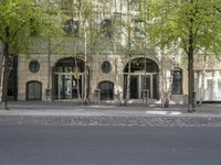 a building with some chairs under it next to the street where there are some trees