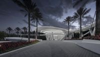 an empty path in front of a modern office building at night with a cloudy sky behind