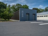 a metal building with a corrugated door in front of it and trees lining the street behind it