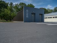 a metal building with a corrugated door in front of it and trees lining the street behind it