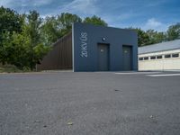 a metal building with a corrugated door in front of it and trees lining the street behind it