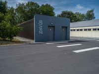 a metal building with a corrugated door in front of it and trees lining the street behind it