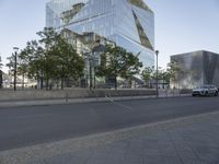 a silver van sits next to trees on the street by a building with glass walls