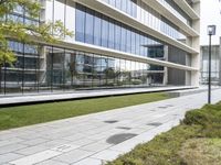 a sidewalk that is surrounded by trees next to an office building with a glass facade