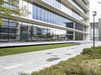 a sidewalk that is surrounded by trees next to an office building with a glass facade