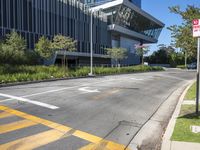 a large modern office building sitting above an empty street near a grassy area and shrubbery