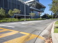 a large modern office building sitting above an empty street near a grassy area and shrubbery