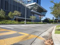 a large modern office building sitting above an empty street near a grassy area and shrubbery