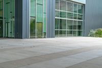 a woman stands on the sidewalk outside an office building that has many windows, and plants around