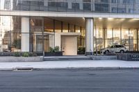 the front entrance of a glass and stone office building in a city with a car parked in front