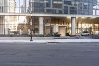 the front entrance of a glass and stone office building in a city with a car parked in front