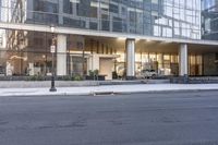 the front entrance of a glass and stone office building in a city with a car parked in front