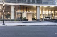 the front entrance of a glass and stone office building in a city with a car parked in front