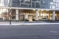 the front entrance of a glass and stone office building in a city with a car parked in front