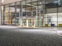 a large modern building at night with cobblestone streets outside it's windows