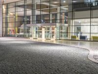 a large modern building at night with cobblestone streets outside it's windows