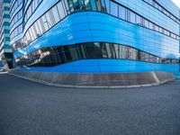 an intersection view of an office building and it's reflection on the pavement while someone is standing next to it