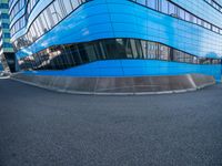 an intersection view of an office building and it's reflection on the pavement while someone is standing next to it