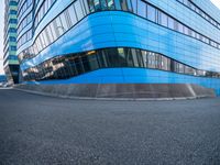 an intersection view of an office building and it's reflection on the pavement while someone is standing next to it