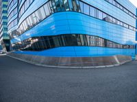 an intersection view of an office building and it's reflection on the pavement while someone is standing next to it