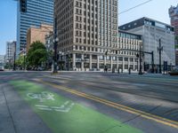 the green paint is painted on a bike path in front of an office building and large, trees