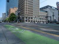 the green paint is painted on a bike path in front of an office building and large, trees