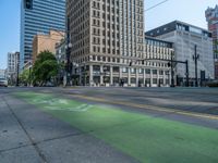 the green paint is painted on a bike path in front of an office building and large, trees