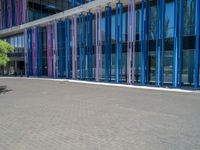 a building with pink glass and purple striped exterior is shown with the brick path on the left