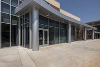 an outside view of a building with a big glass window and concrete flooring on the ground