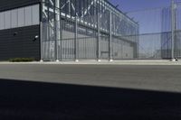 a black building with metal fence near an empty parking lot of concrete streets and street lights