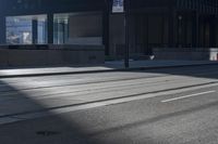 the road on a sunny day with shadows of buildings in front of it and a traffic light