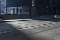 the road on a sunny day with shadows of buildings in front of it and a traffic light