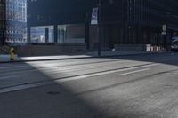 the road on a sunny day with shadows of buildings in front of it and a traffic light