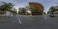 a long curved building with people walking on the sidewalk on both sides of it and a van driving past it