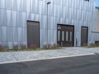 a black fire hydrant stands outside a building with metal cladding and plants in front